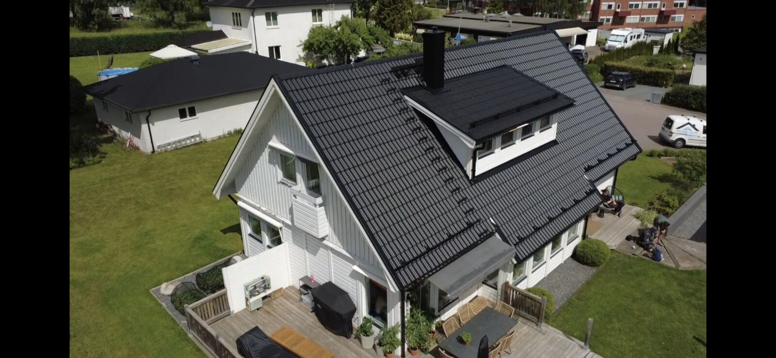 Drönarfoto, svart tegeltak på vitt hus med trädäck