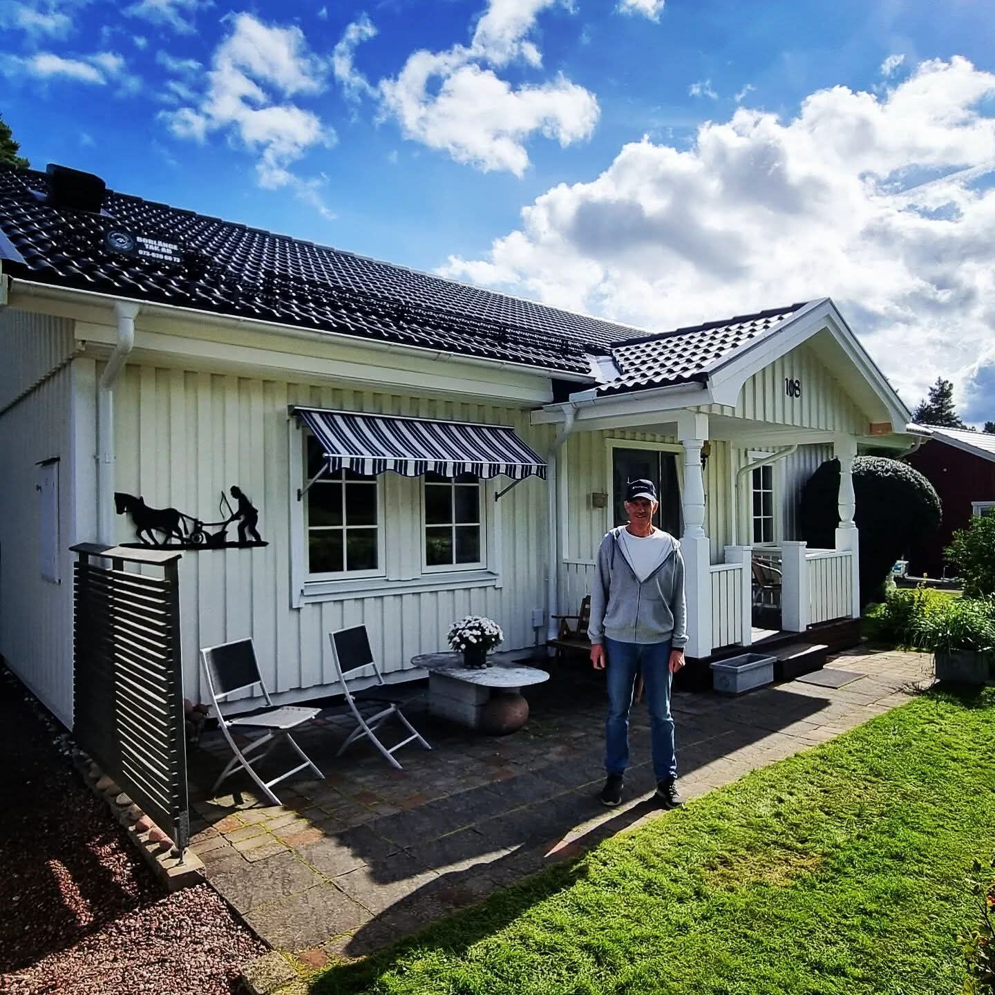 Nöjd kund framför vitt hus med nytt svart tegeltak